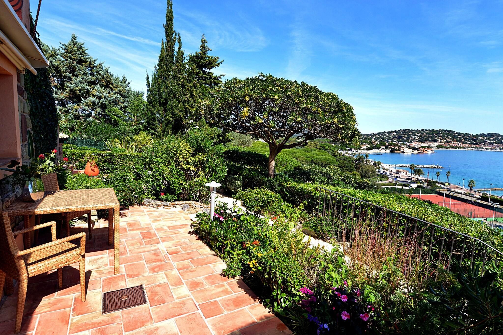 A patio with a table and chairs, surrounded by lush greenery and a view of the sea.