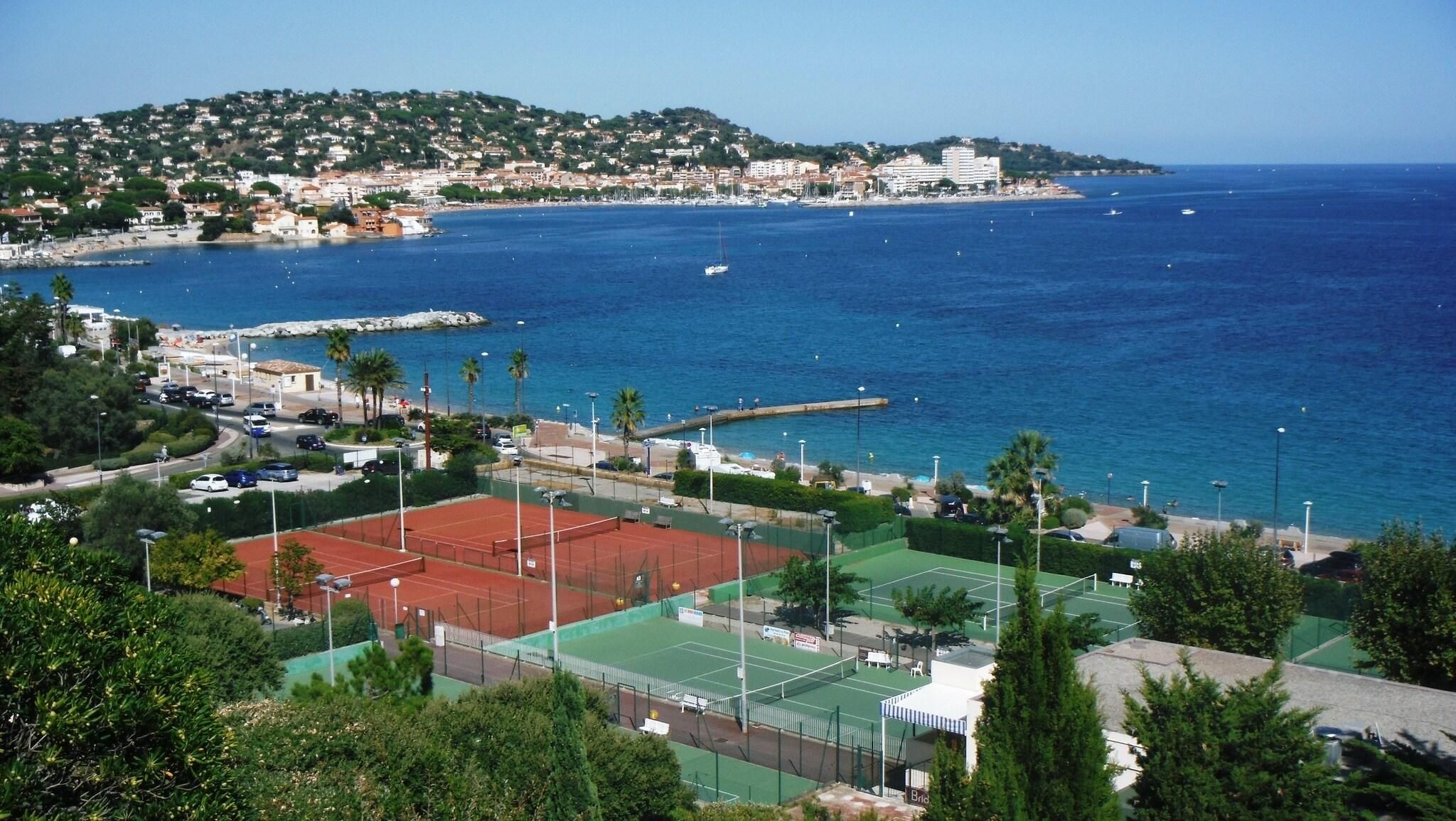 A coastal town with a tennis court, a marina, and a hillside with buildings.