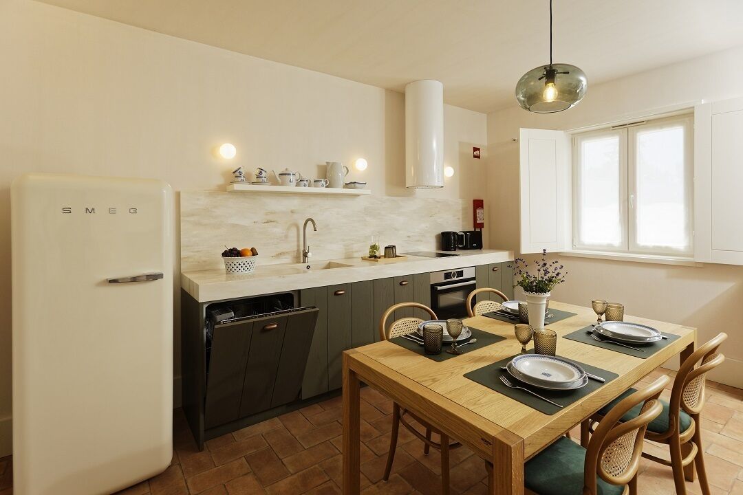 Cocina compacta con refrigerador blanco, horno empotrado y pileta. Se observa una mesa de comedor con platos y cubiertos.