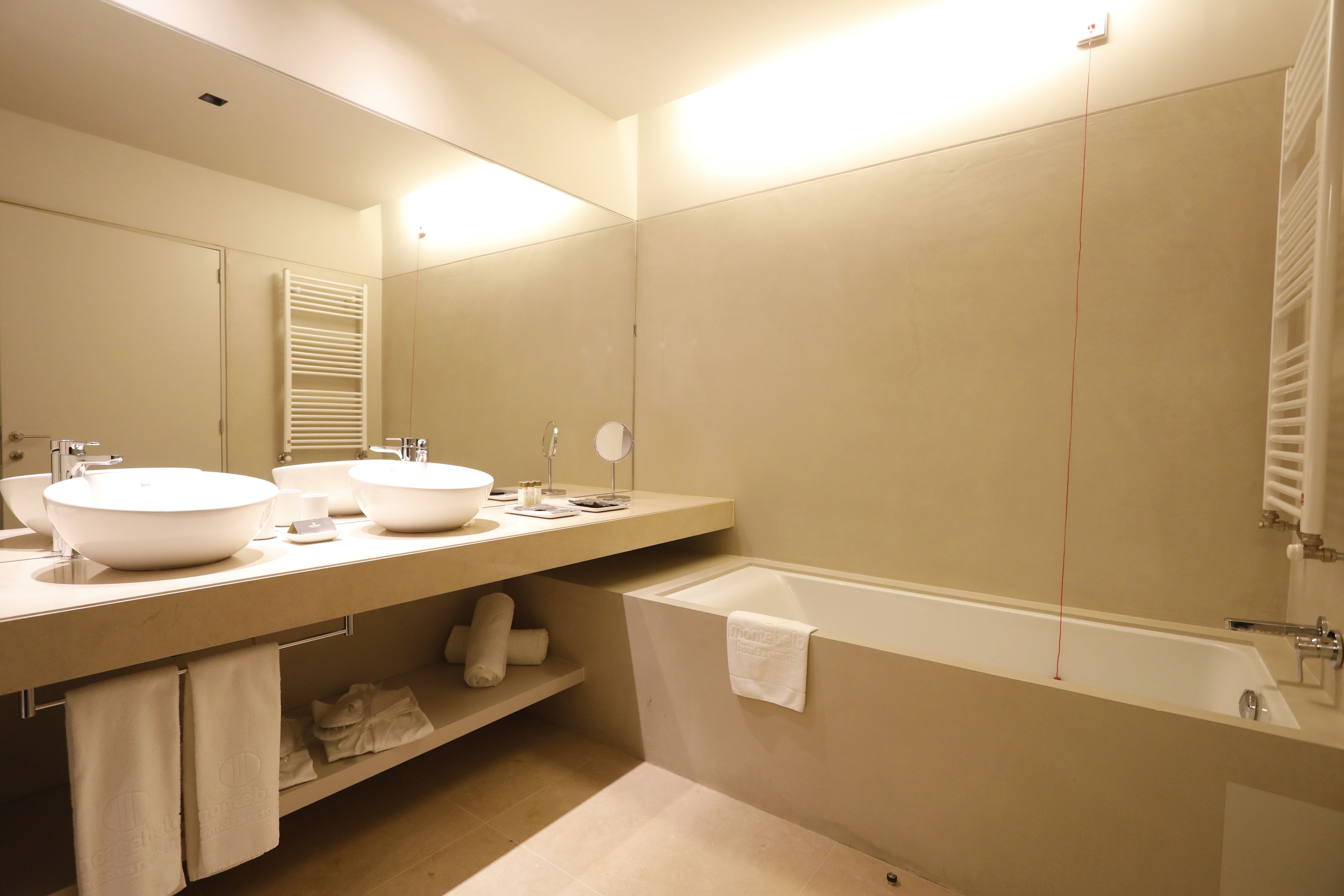 A modern bathroom with two sinks, a bathtub, and a large mirror.