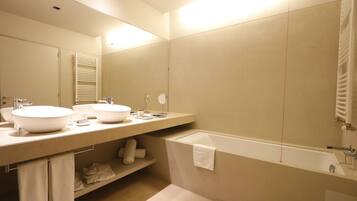 A modern bathroom with two sinks, a bathtub, and a large mirror.