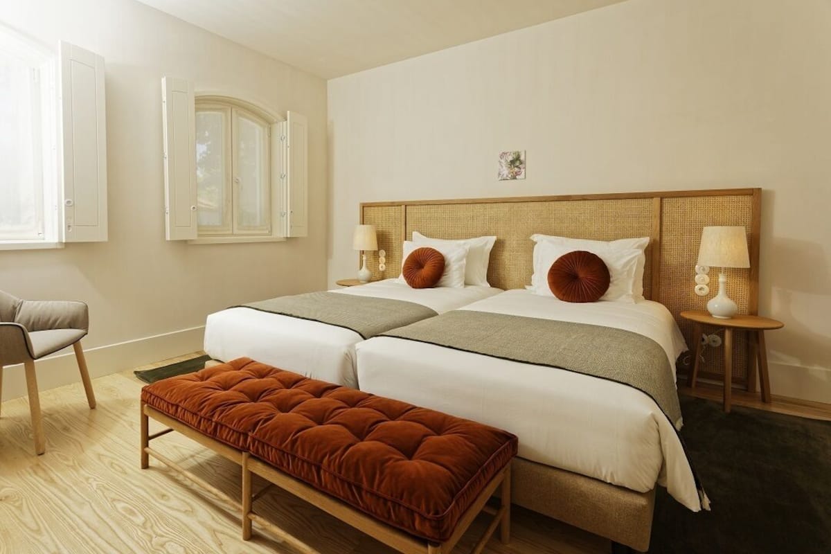 A double bed with a wooden headboard, two bedside tables with lamps, a bench, and a chair.