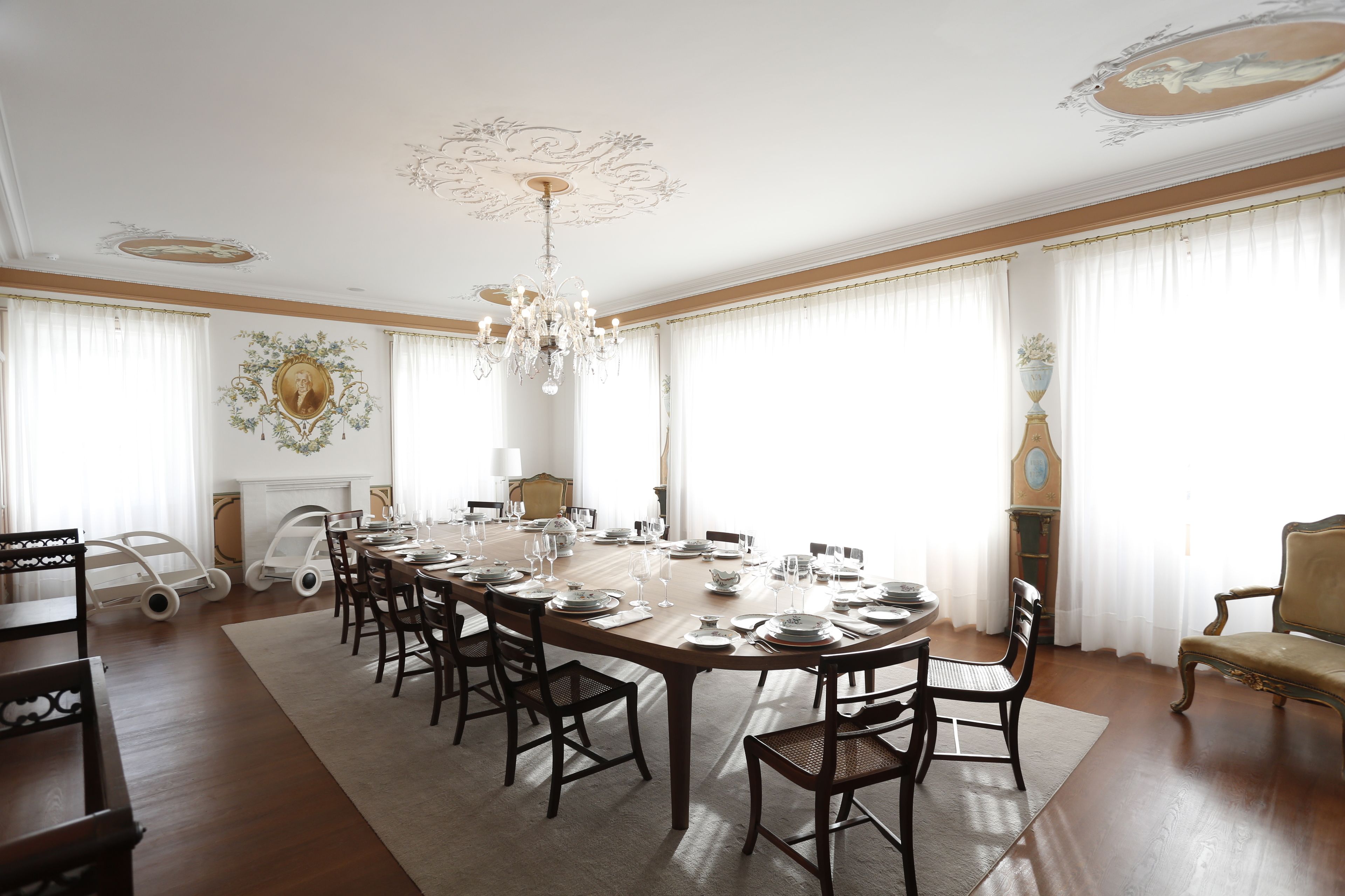 A formal dining room with a long table set for a meal, surrounded by chairs, and a chandelier.