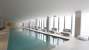 A modern indoor swimming pool with a long, narrow design, surrounded by white sofas and chairs, and large windows providing natural light. - Montebelo Vista Alegre Ílhavo Hotel (Ilhavo)