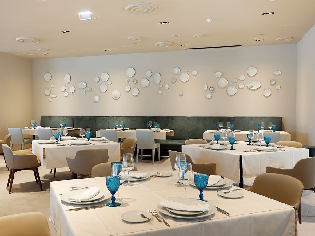 Un comedor con mesas dispuestas para el servicio, una pared con diseños circulares e iluminación empotrada en el techo.