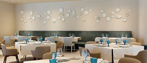 Un comedor con mesas dispuestas para el servicio, una pared con diseños circulares e iluminación empotrada en el techo.