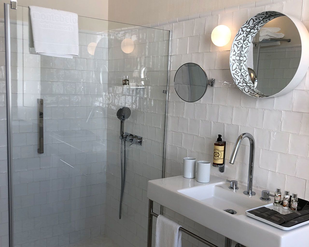 Une salle de bain moderne avec une douche à parois de verre, un lavabo blanc avec un miroir au-dessus et un porte-serviettes.