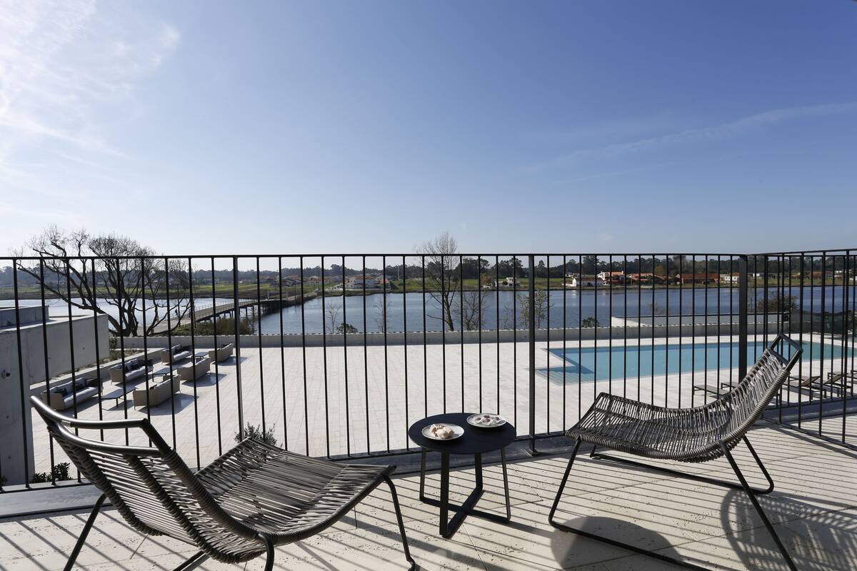 A balcony with a pool view, two lounge chairs, and a small table with plates.
