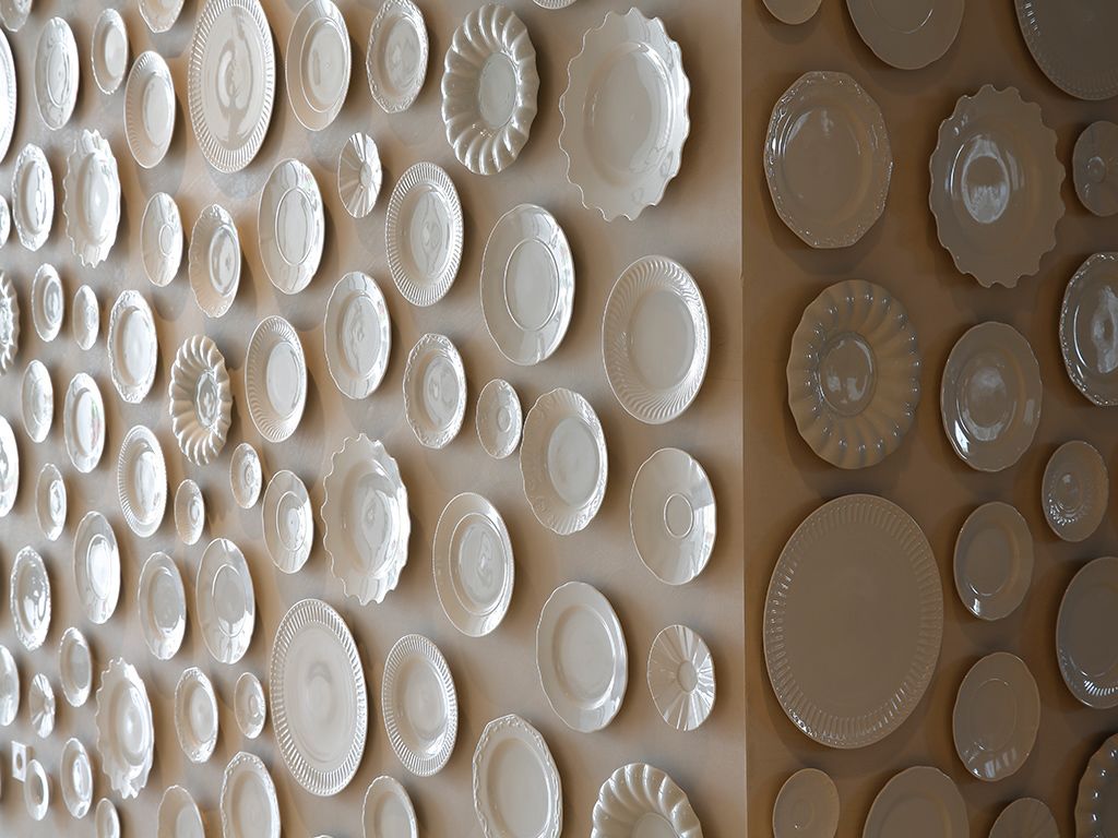 A wall with numerous white plates of various shapes and sizes.