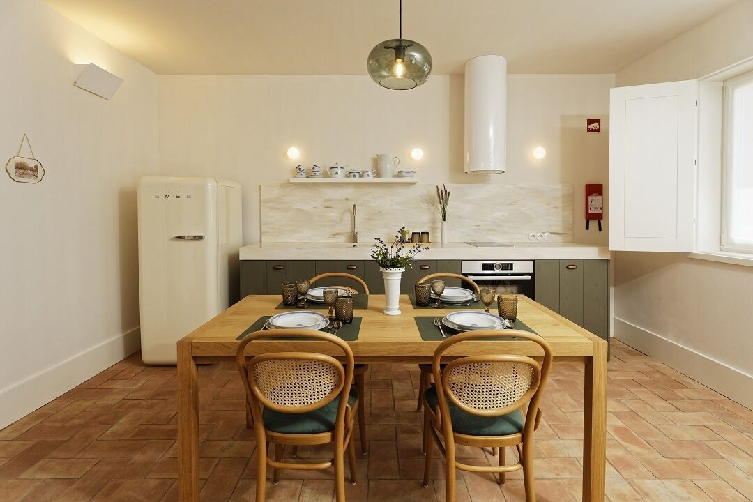 A compact kitchen with a dining table set for four, equipped with a refrigerator, a stove, and a hanging light fixture.
