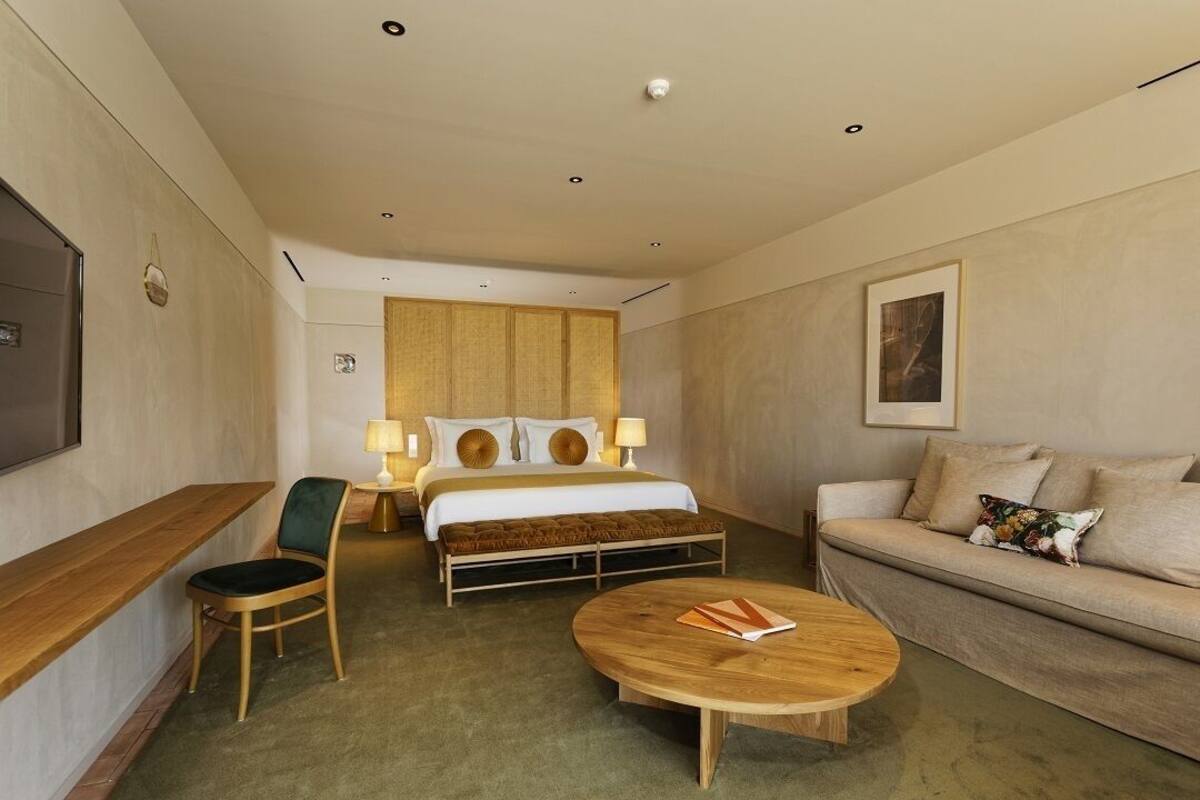 A hotel room with a bed, a sofa, a chair, a coffee table, and a TV.