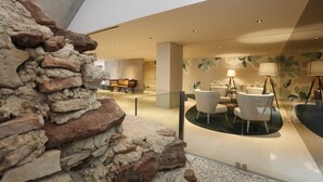 A modern interior with a stone wall, seating area with chairs and a table, and a decorative wall with leaf patterns. - Montebelo Vista Alegre Ílhavo Hotel (Ilhavo)