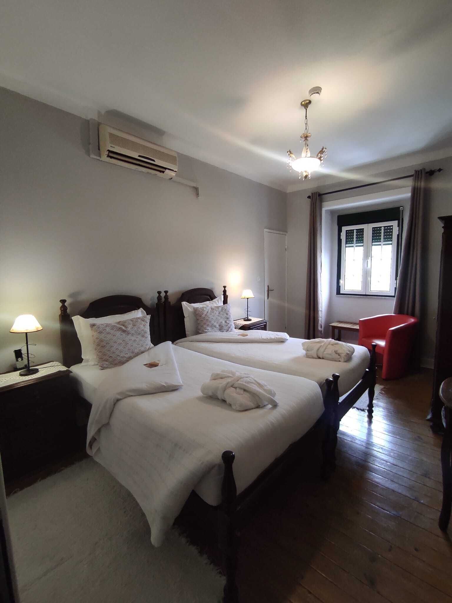 Habitación de hotel con dos camas, una silla roja, una lámpara de araña y un equipo de aire acondicionado.