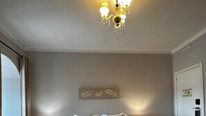 A hotel room with a large bed, two bedside tables with lamps, a chandelier, a door with a lock, and a window with curtains. - Hotel Boavista - Vintage House (Idanha-a-Nova)