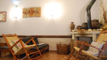 Une pièce chaleureuse avec une cheminée, des fauteuils à bascule en bois, un canapé et des œuvres d’art accrochées aux murs.