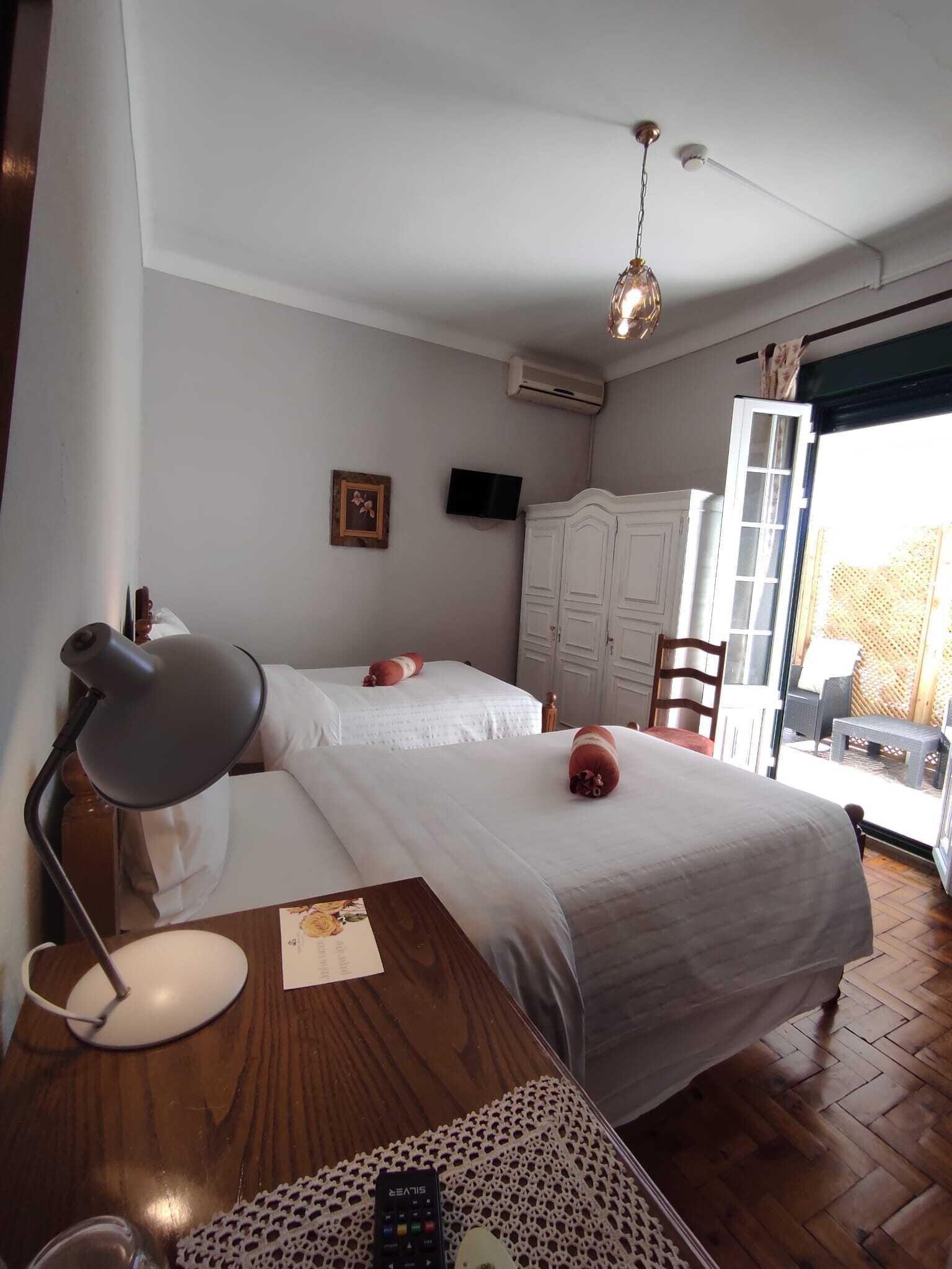 A hotel room with two beds, a desk with a lamp, a television, and a view of the outdoors.