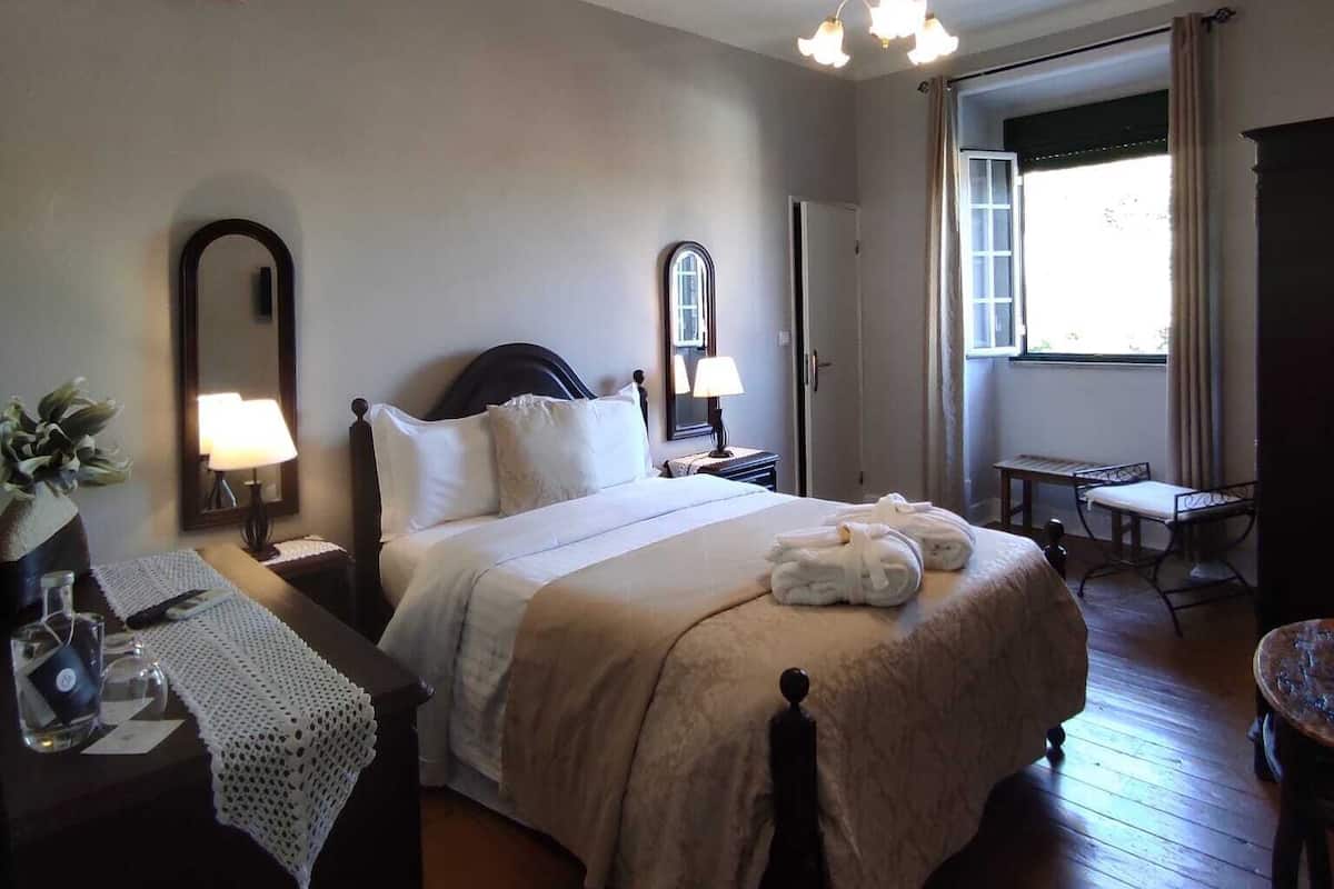 A hotel room with a bed, bedside tables, a mirror, a window, and a door.