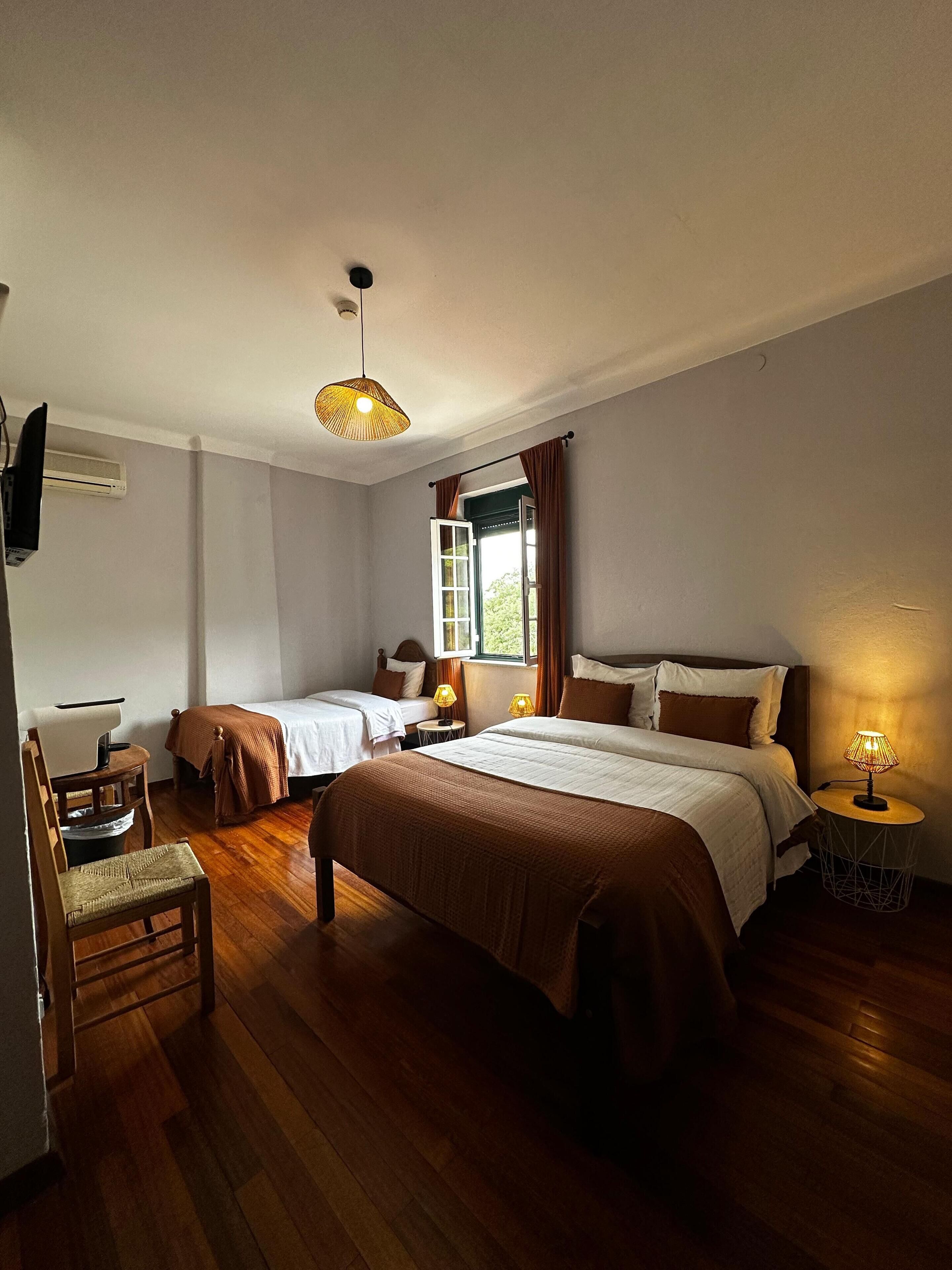 Camera d'albergo con due letti, una scrivania, una sedia, una TV e una finestra con tende.