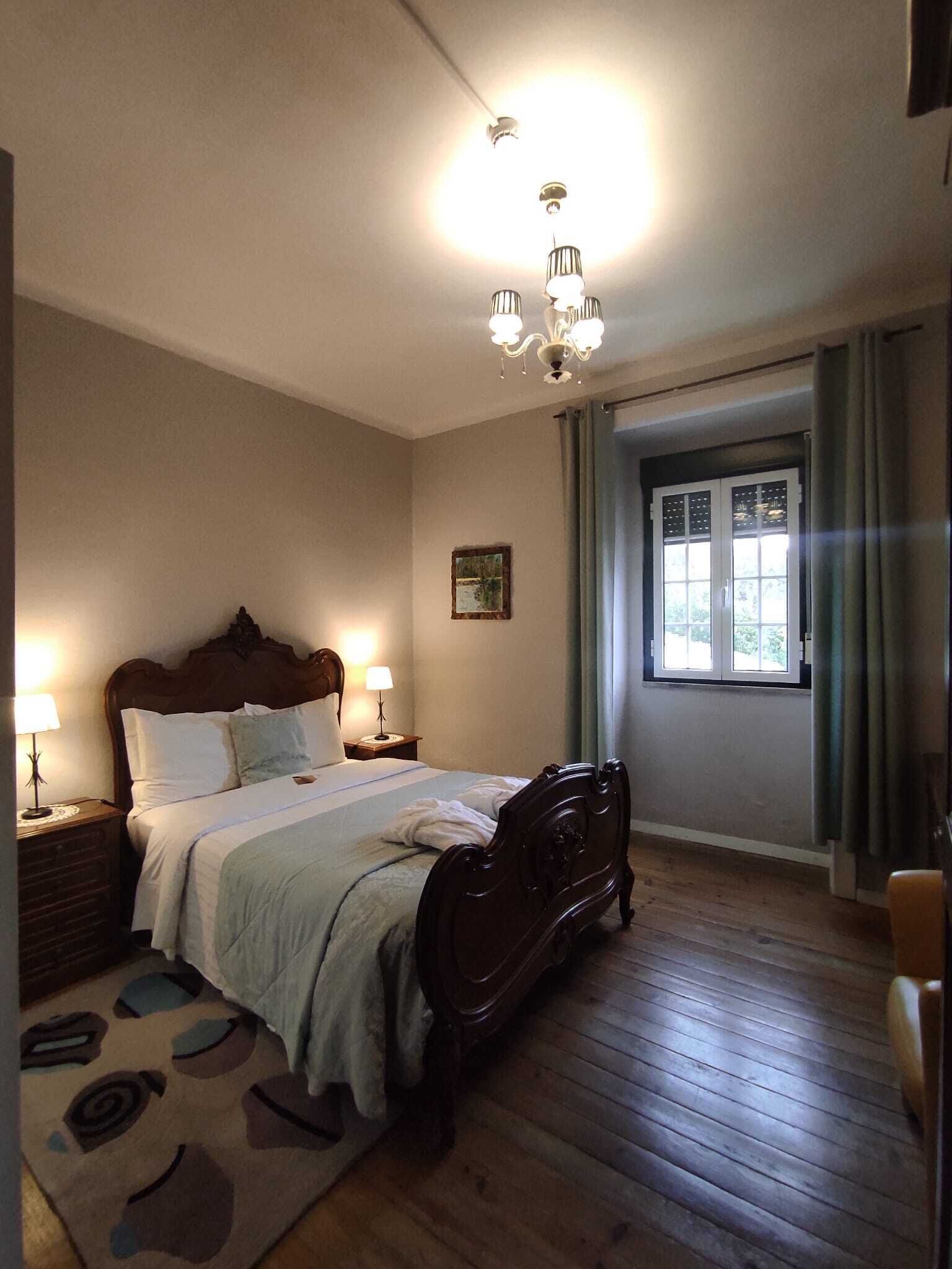 Une chambre à coucher avec un lit en bois, deux lampes de chevet, une fenêtre avec des rideaux et un plancher en bois.