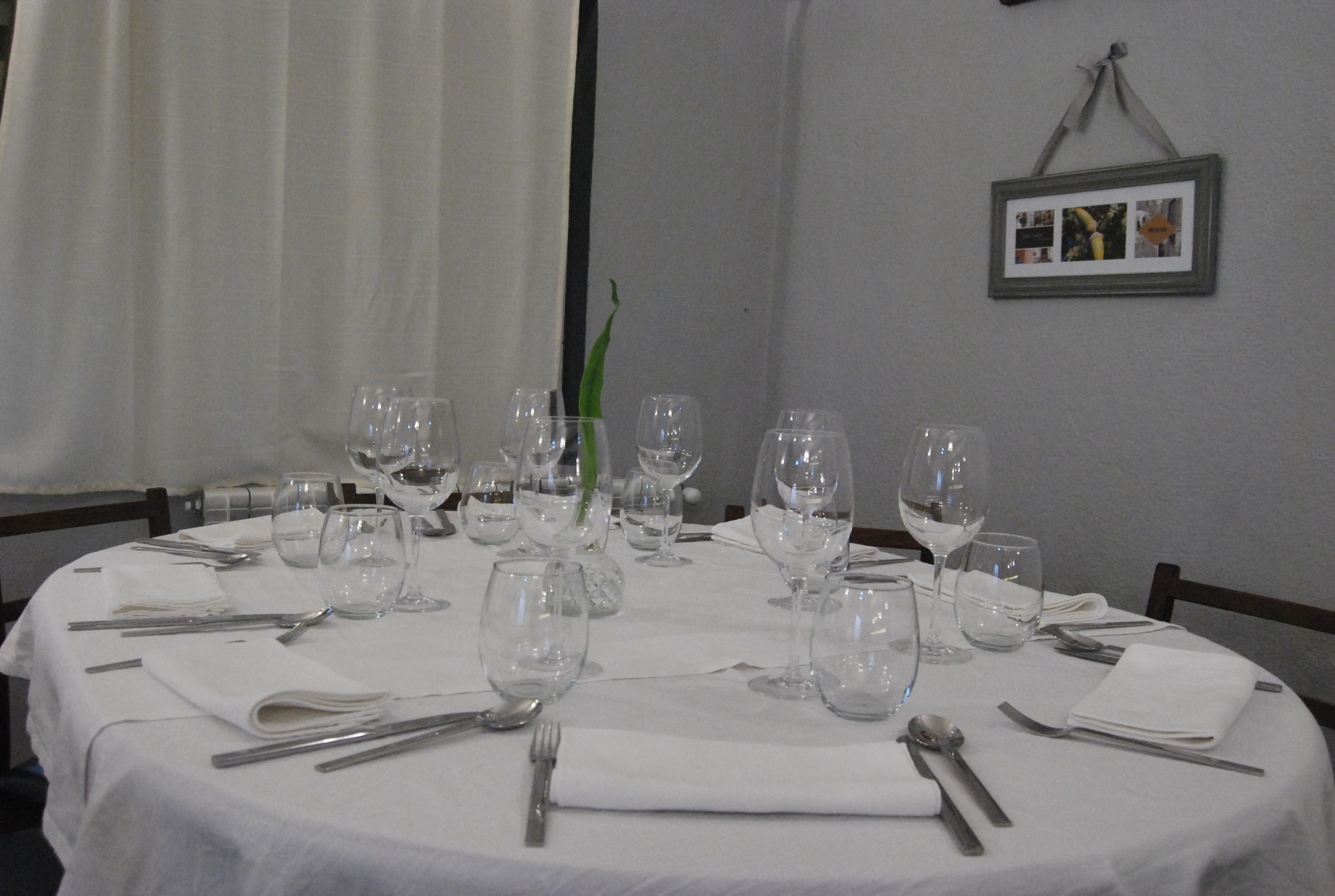 Una mesa redonda para comer dispuesta con varias copas de vino, platos y cubiertos, con un marco con una fotografía en la pared.