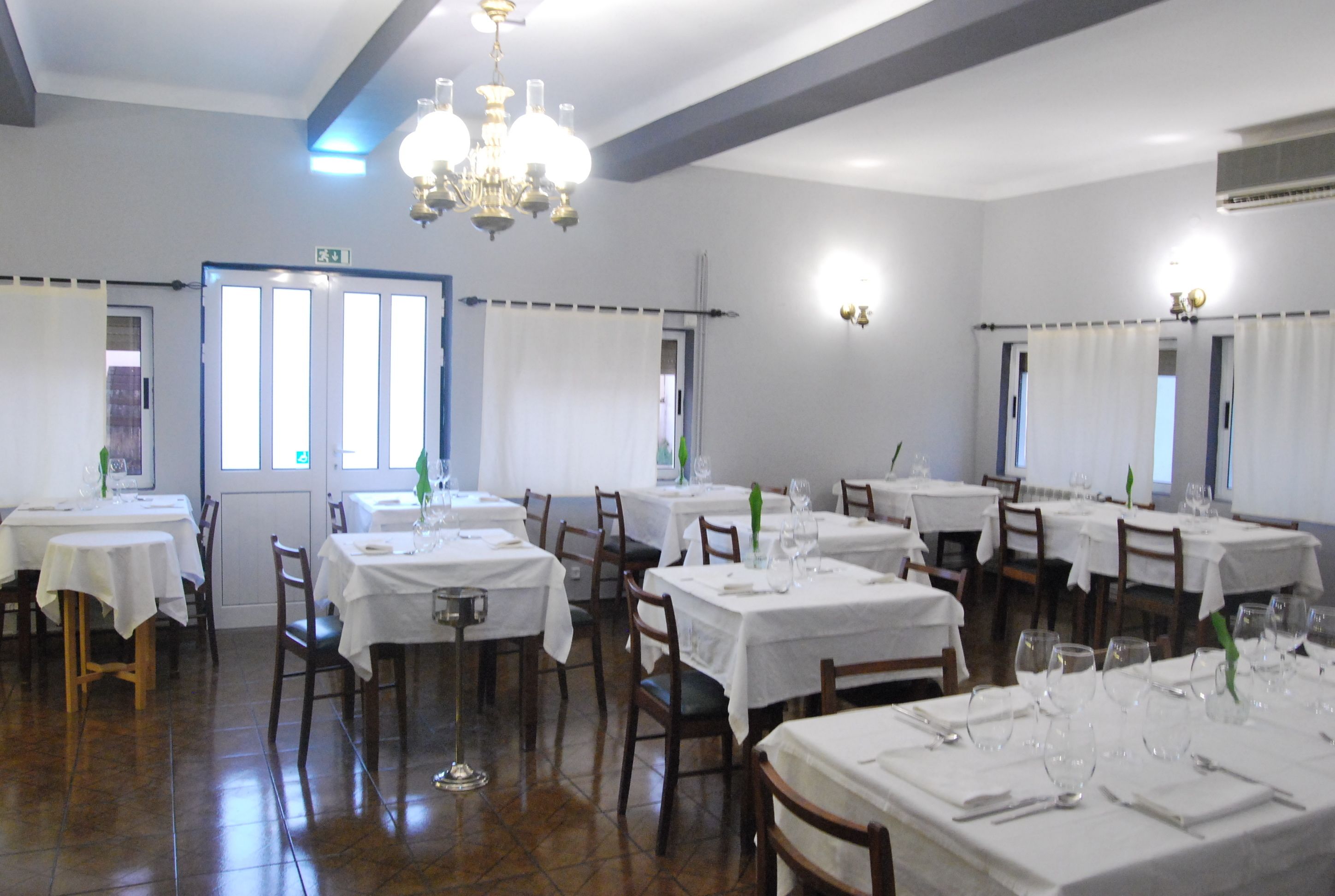 Un comedor con varias mesas dispuestas para el servicio, cada una con manteles blancos y cubertería.