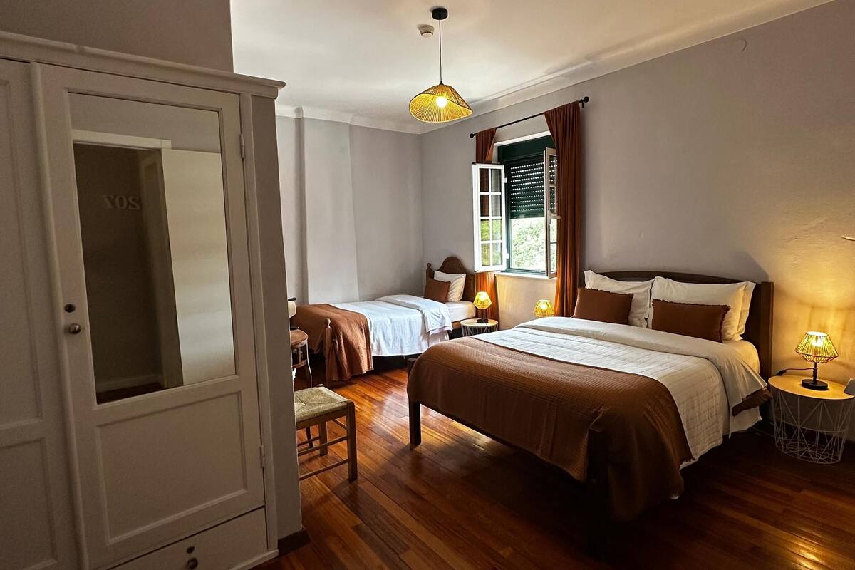 A bedroom with two beds, wooden flooring, a wardrobe, and a window with curtains.