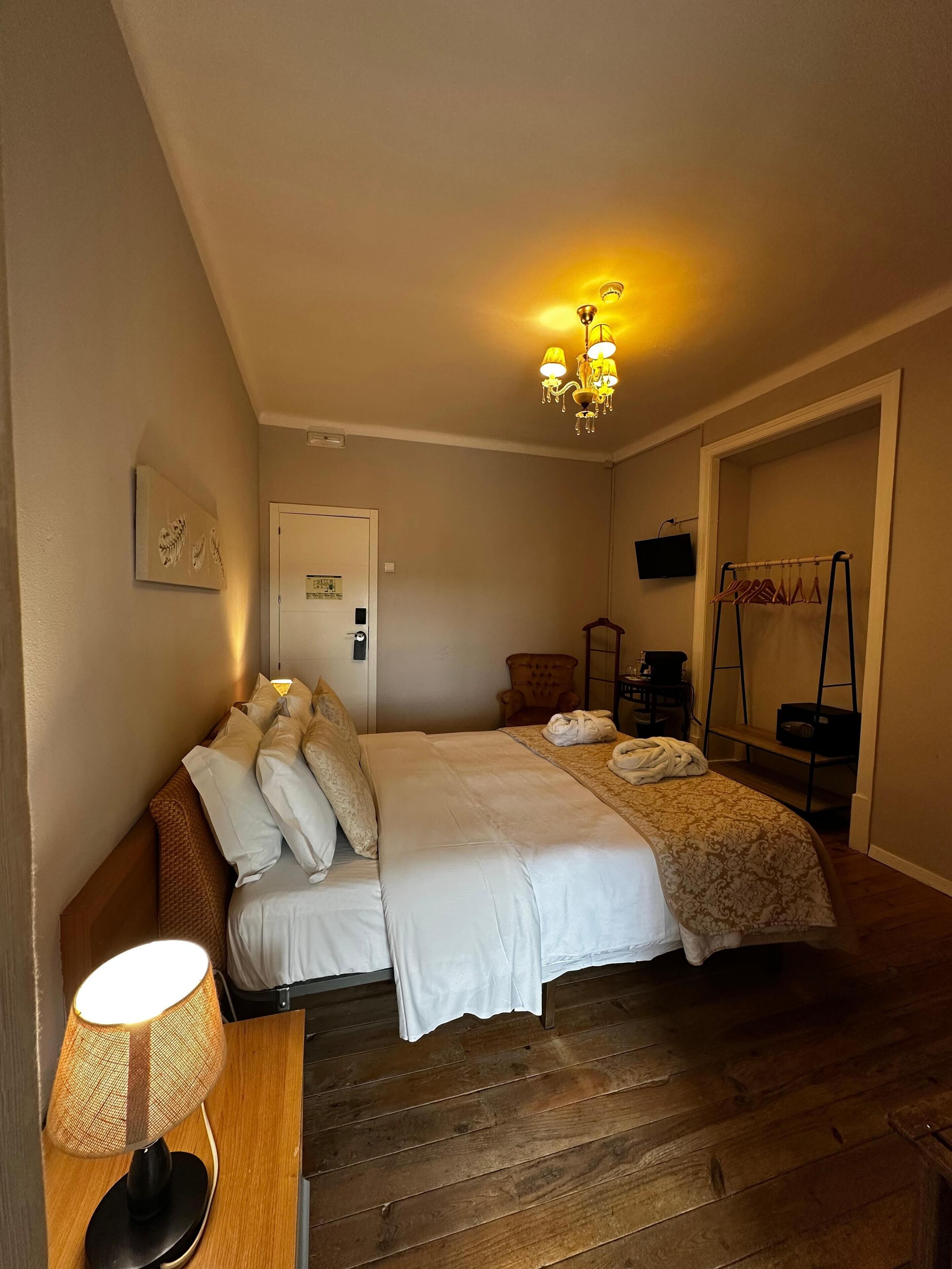 A bedroom with a bed, a lamp, a chair, a TV, and a coat rack.