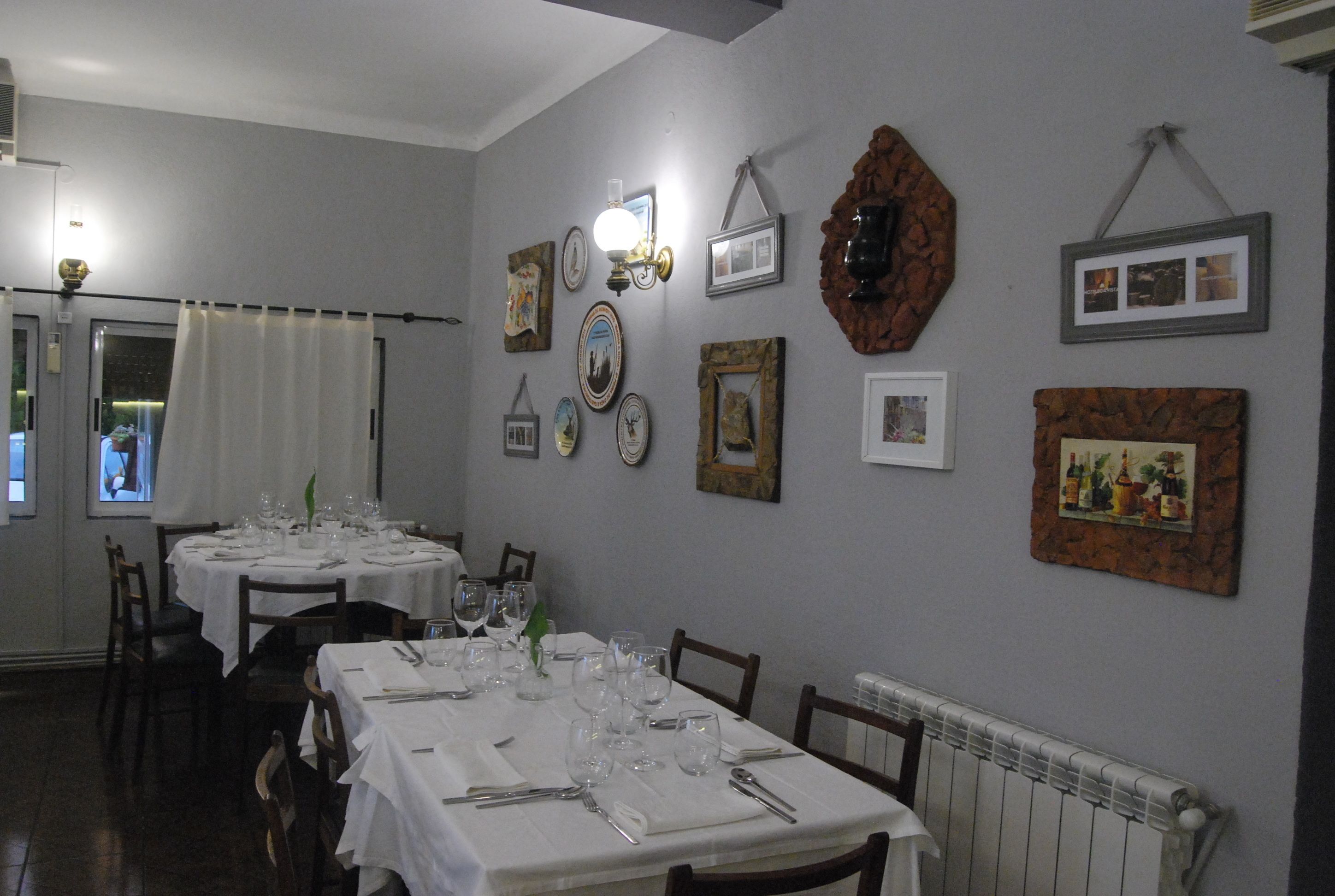 A dining area with tables set for a meal, framed pictures on the walls, and a radiator below.