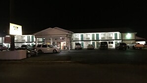 Un motel con varias habitaciones, un estacionamiento y un letrero que indica un área de recepción.