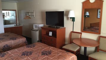 Habitación de hotel con dos camas, televisión, refrigerador pequeño, escritorio con lámpara y espejo.