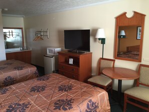 A hotel room with two beds, a TV, a small fridge, a desk with a lamp, and a mirror.