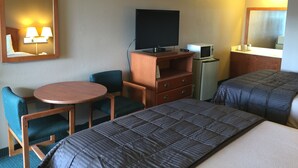 Habitación de hotel con cama, escritorio con silla, televisión, microondas y espejo.