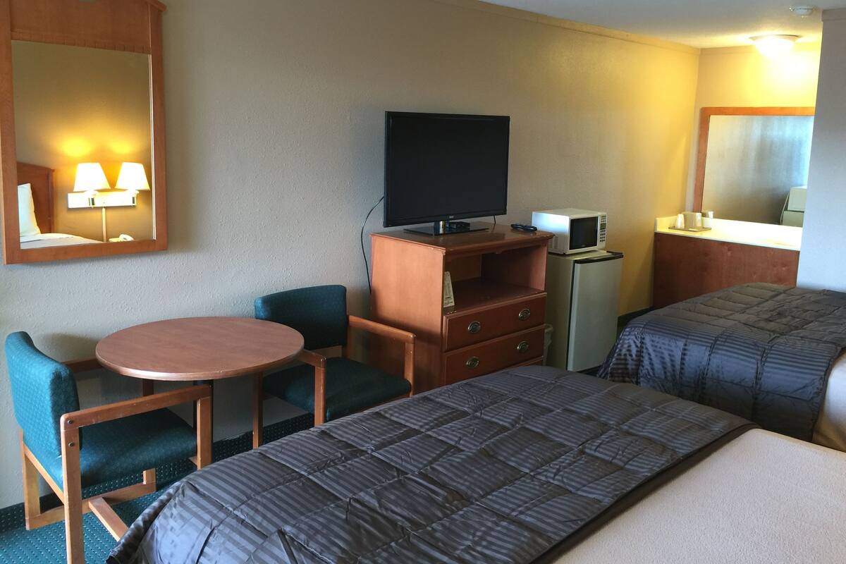 A hotel room with a bed, a desk with a chair, a television, a microwave, and a mirror.