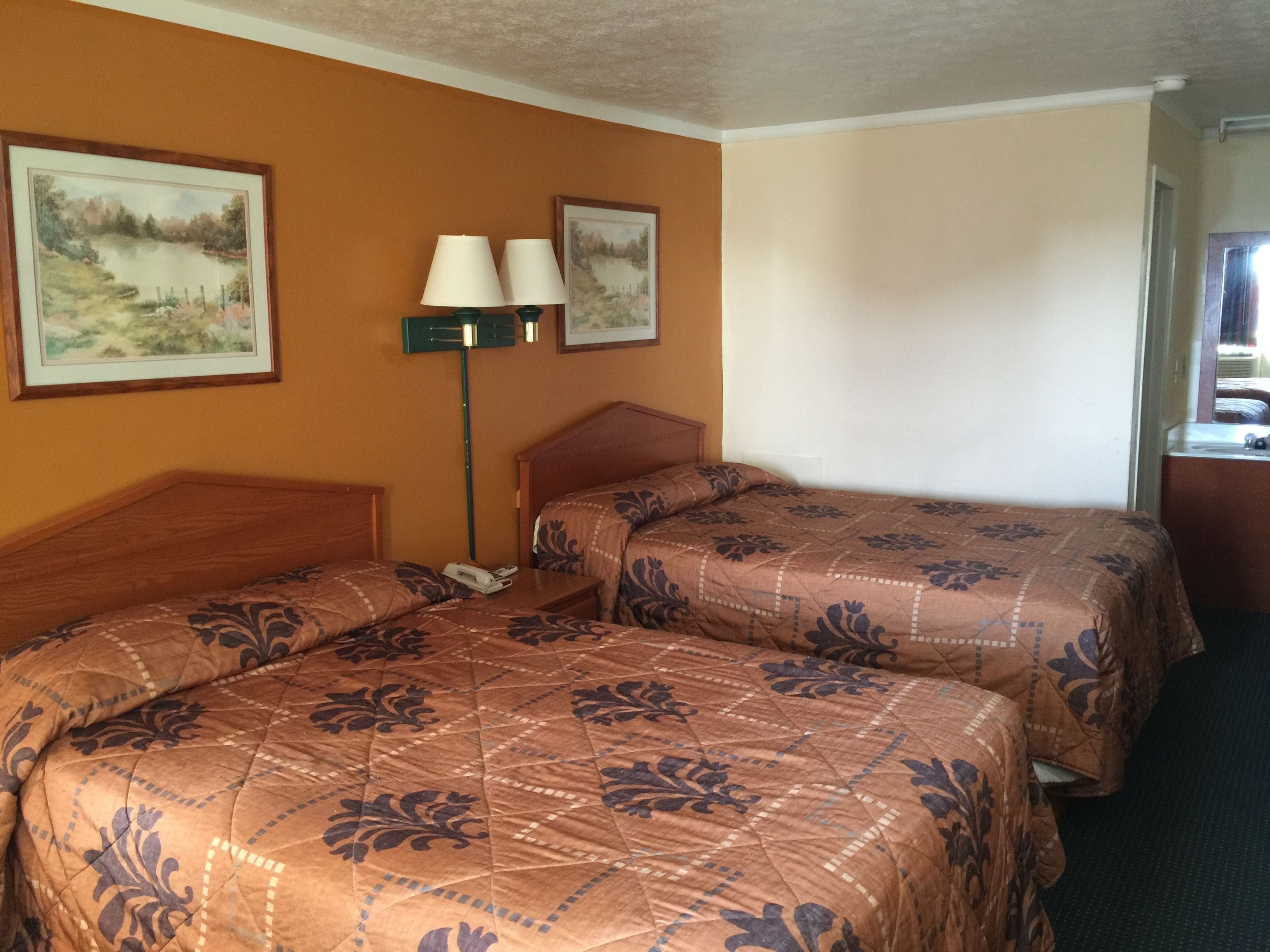 A hotel room with two beds, a nightstand, a lamp, and two framed pictures on the wall.
