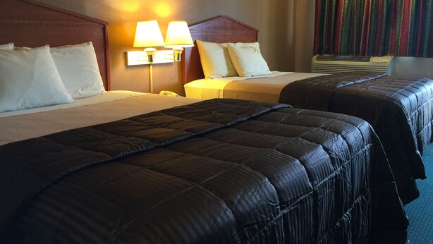 Una habitación de hotel con dos camas, cada una con cabecero, mesita de noche y lámpara.