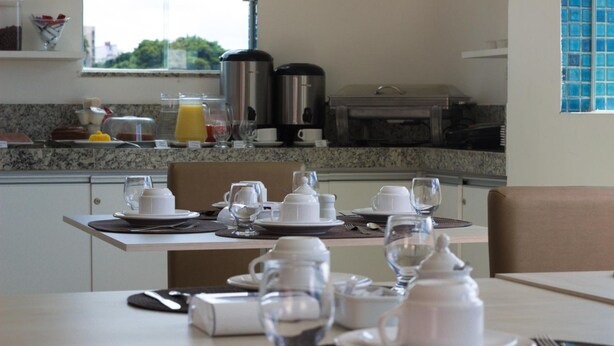 A breakfast setup with a table set for two, including plates, cups, and a coffee maker. - Aquarena Hotel (Salvador)