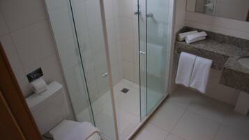 A modern bathroom with a glass-enclosed shower, a toilet, and a granite countertop with a sink and towel rack.