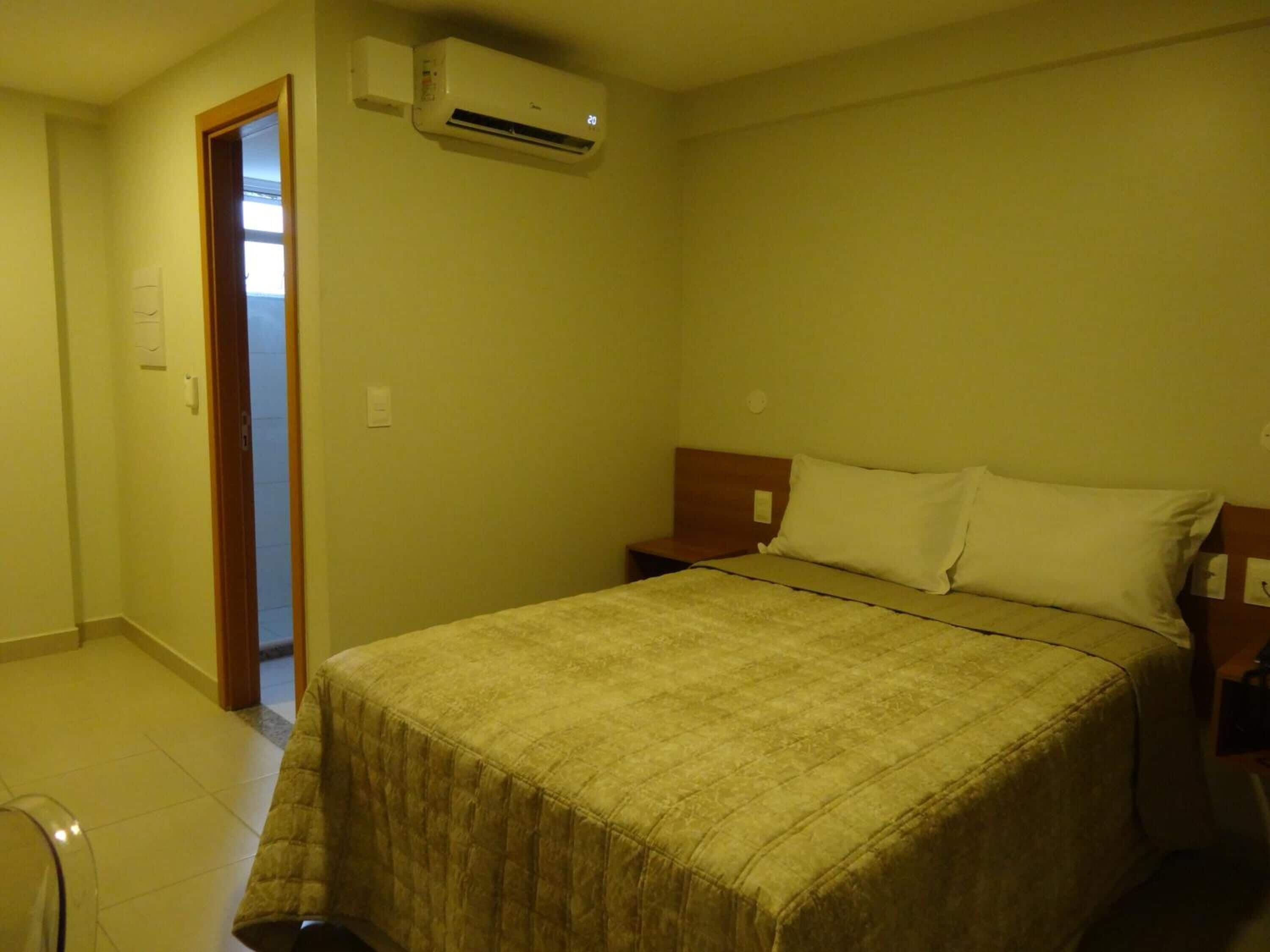 Quarto de hotel com cama, mesa de cabeceira e ar condicionado.