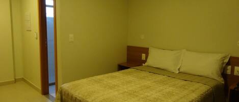 A hotel room with a bed, bedside table, and an air conditioning unit.