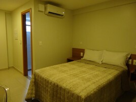 Una habitación de hotel con cama, mesita de noche y aire acondicionado.