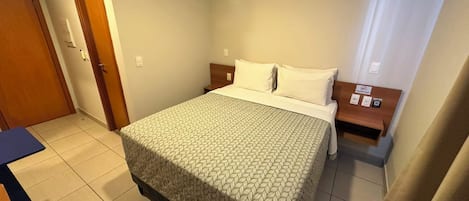Una camera d'albergo con un letto, un comodino, un condizionatore d'aria, una porta e un bagno.
