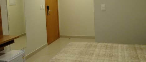 A bedroom with a bed, a wooden door, an air conditioner, and a small white appliance on the floor.