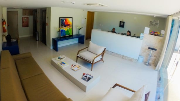 Un vaste espace de vie comprenant un canapé, une table basse avec des magazines, un tableau coloré et un comptoir d’accueil avec du personnel.