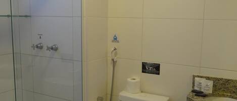 Un baño con cabina de ducha de vidrio, inodoro y lavamanos con toallero.