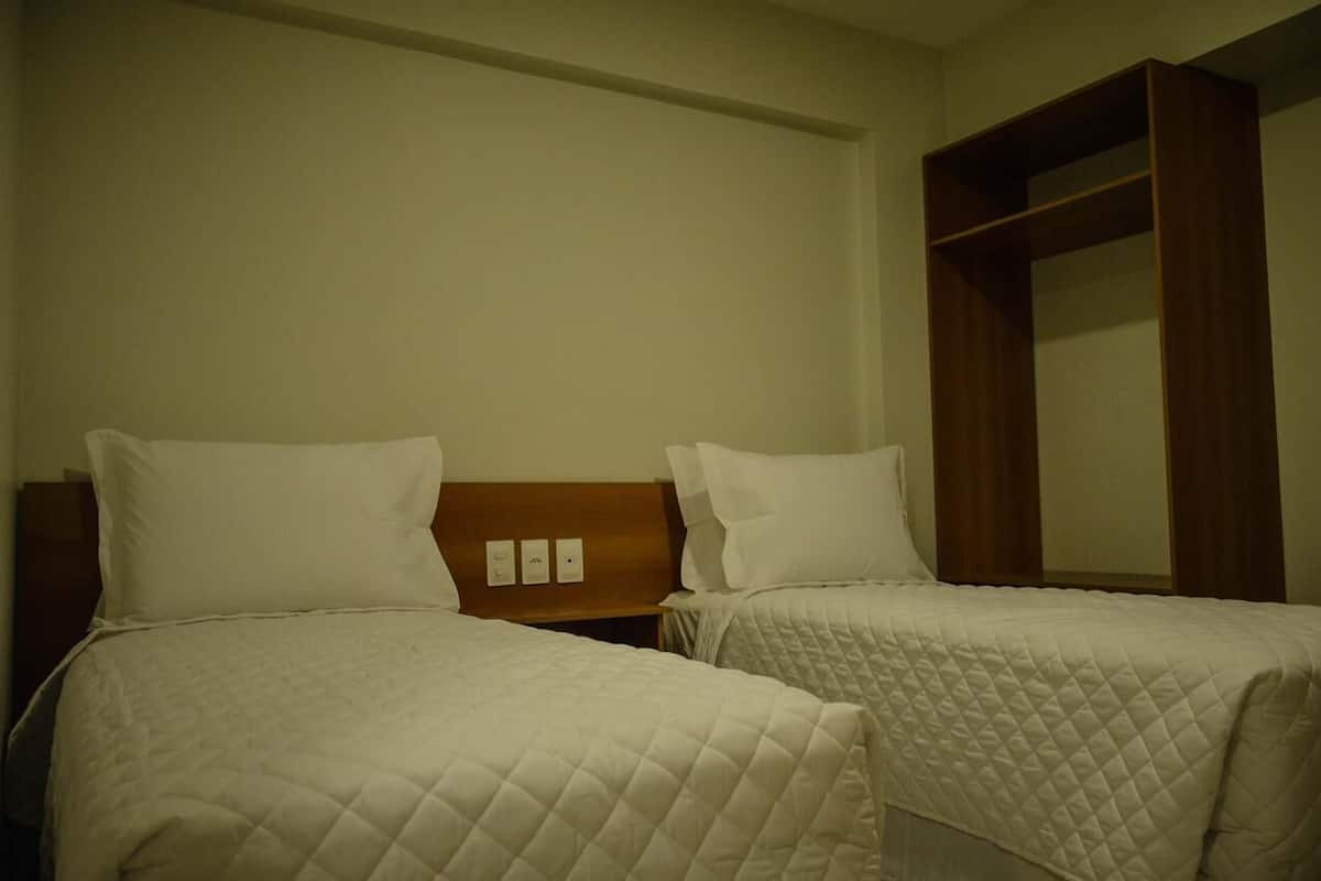 Habitación de hotel con dos camas individuales, cabecera de madera y un amplio armario.