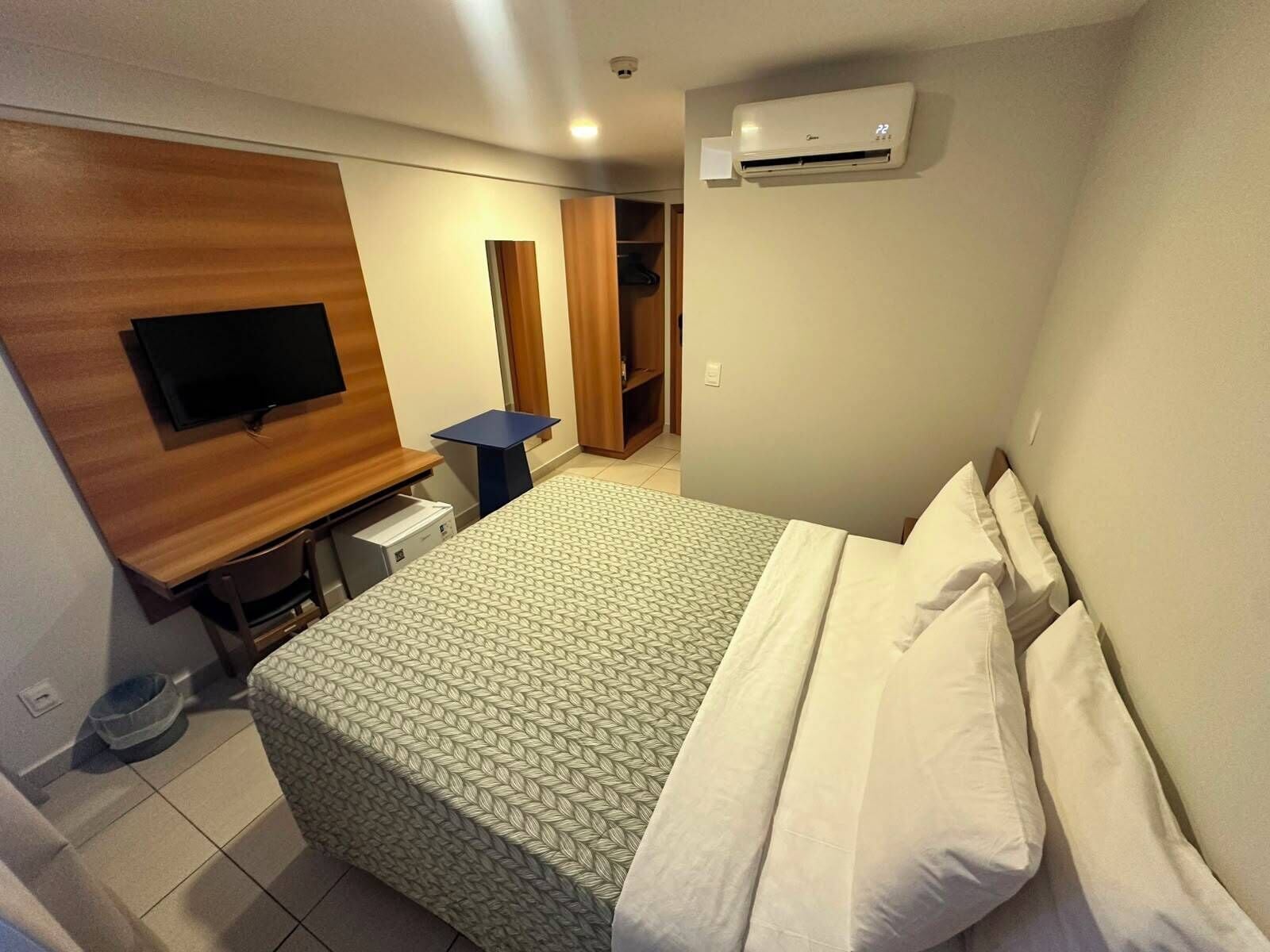 Una habitación de hotel con cama, televisión, escritorio y aire acondicionado.
