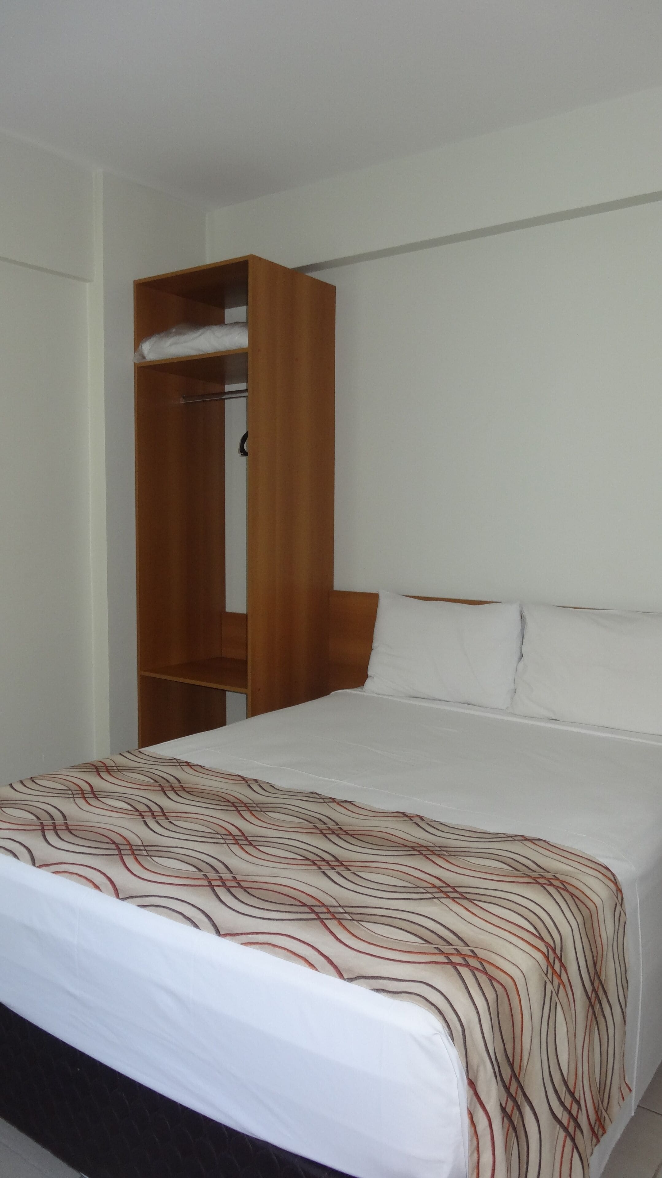 A bedroom with a bed, a wooden wardrobe, and a white wall.
