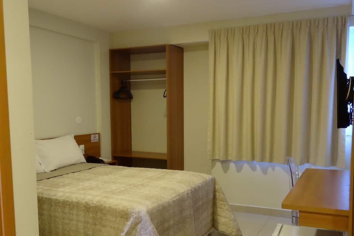 Una habitación de hotel con una cama, un armario de madera, una mesita y un refrigerador blanco.