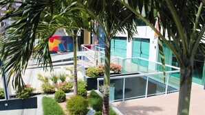 A modern outdoor area with a pool, palm trees, and a colorful mural on a building. - Aquarena Hotel (Salvador)