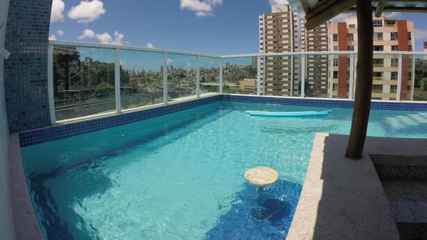 Piscina en la azotea con agua azul cristalina, rodeada por una barandilla de vidrio, bajo una estructura de techo metálico.